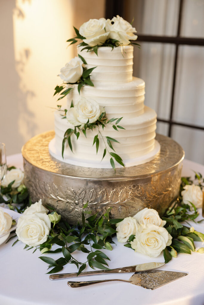 White tiered wedding cake with flowers and greenery.