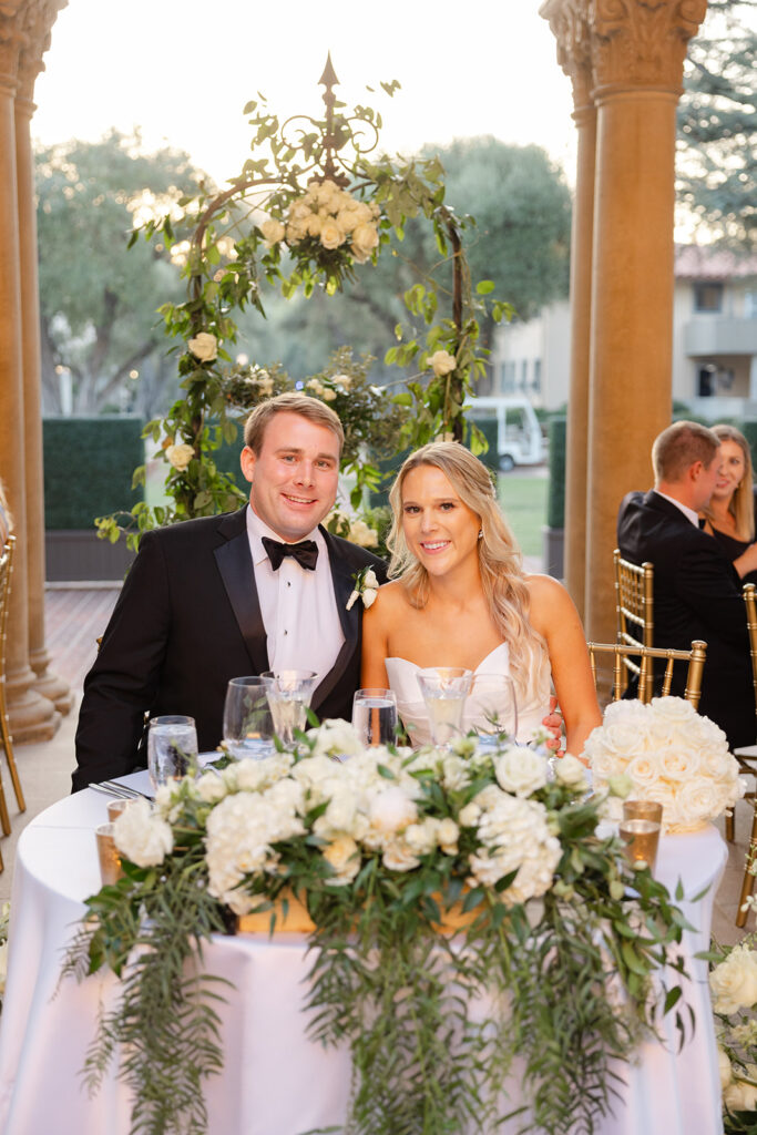 Ben and Kelly smiling together at their wedding reception table.