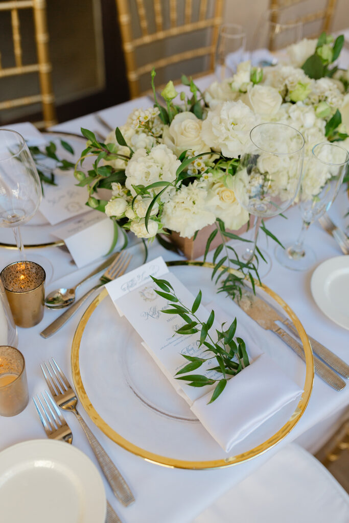 White flowers, gold flatware, and glassware on a wedding reception table.