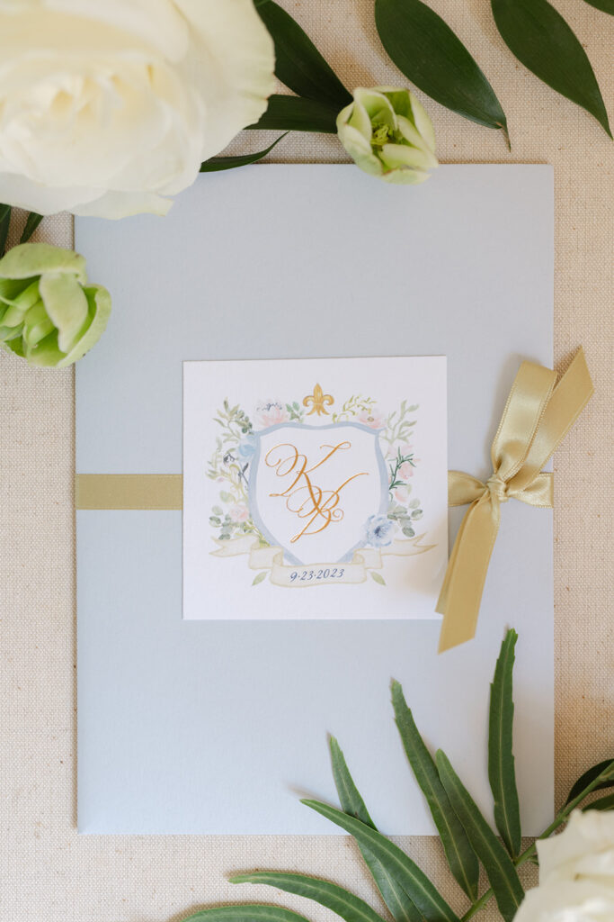Ben and Kelly’s wedding invitation with a decorative monogram and gold ribbon.