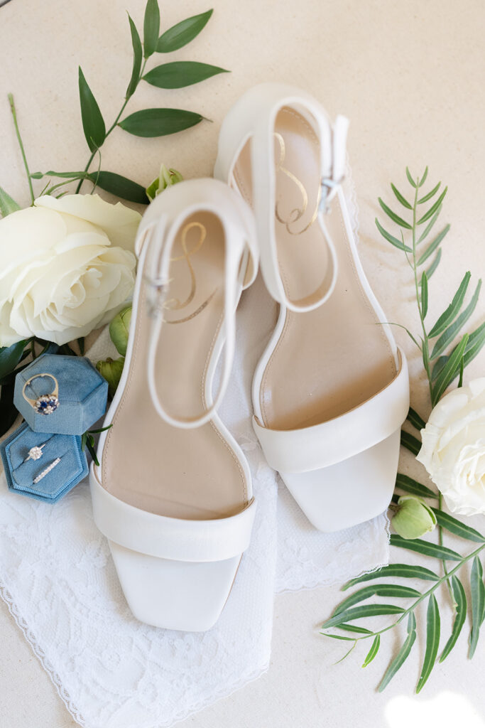White bridal shoes arranged with roses and greenery.