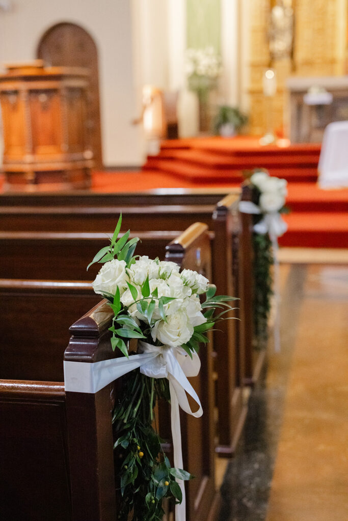 White flowers and greenery decorating a wooden pew at Holy Family Church.