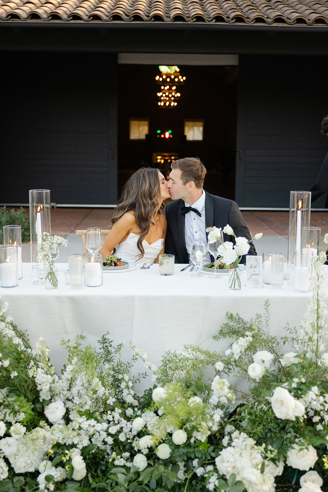 Jake and Zoe kissing at their flower-lined sweetheart table.