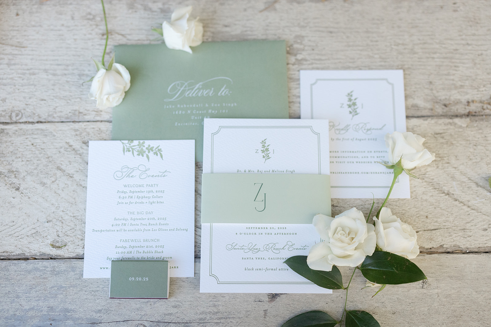 White and sage-green wedding invitations arranged with white roses on a wooden table.