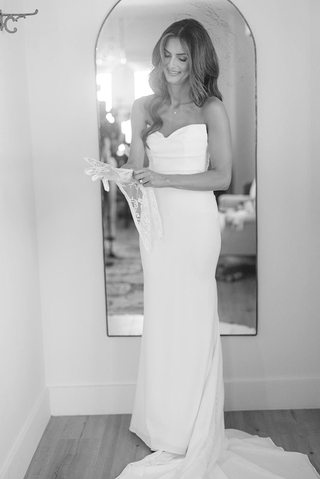 Zoe reflected in an arched mirror in her wedding dress, in black and white.
