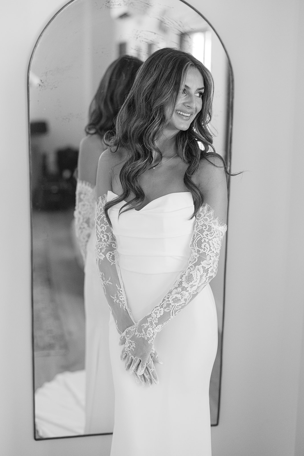 Black-and-white bridal portrait of Zoe in lace sleeves beside a mirror.