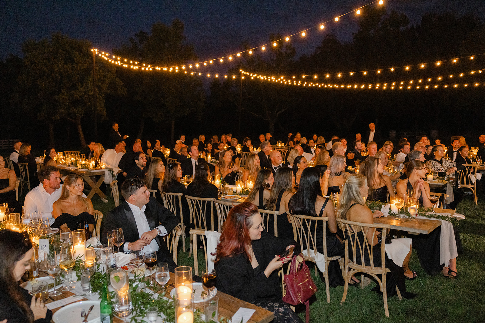 Wedding guests raising their glasses beneath glowing string lights at night.