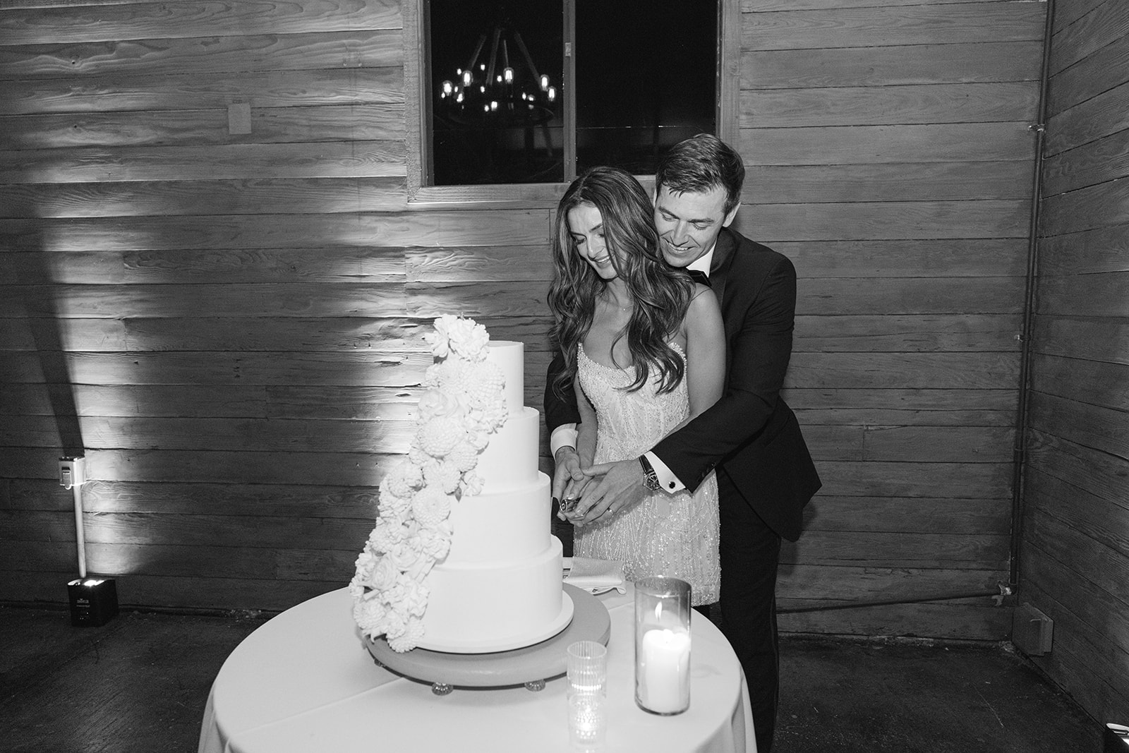 Jake and Zoe cutting their wedding cake together, in black and white.