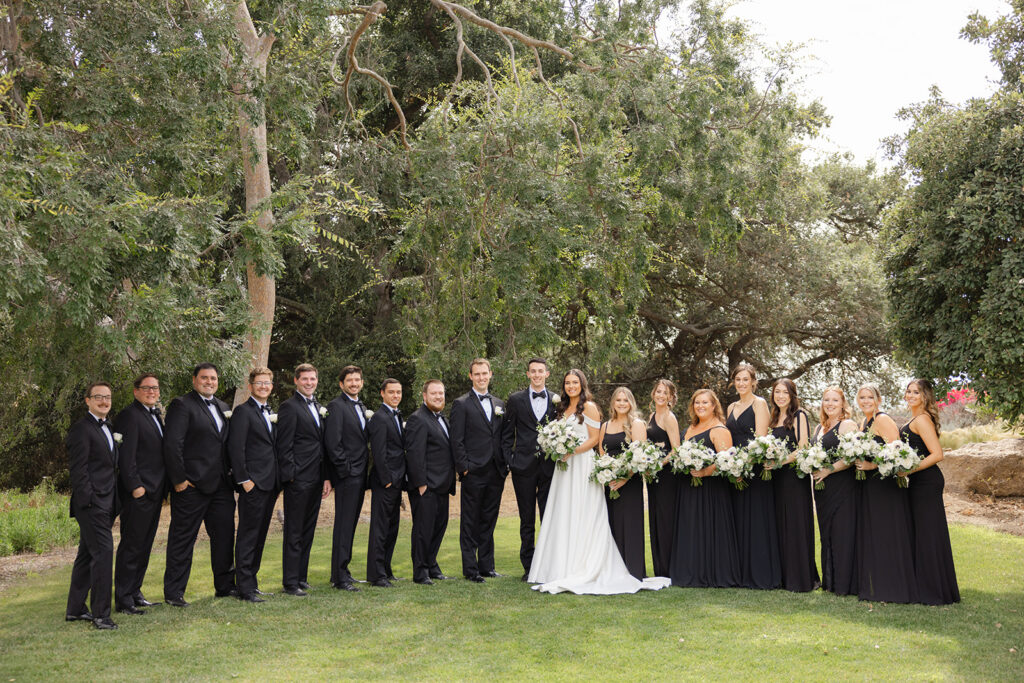 Samantha and Andrew with their wedding party in black attire on the garden lawn.