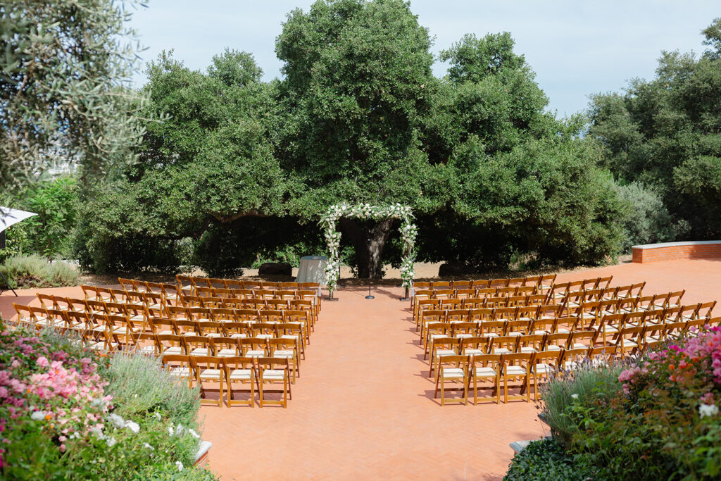 Outdoor ceremony chairs and white floral arbor beneath the oak at Quail Ranch.