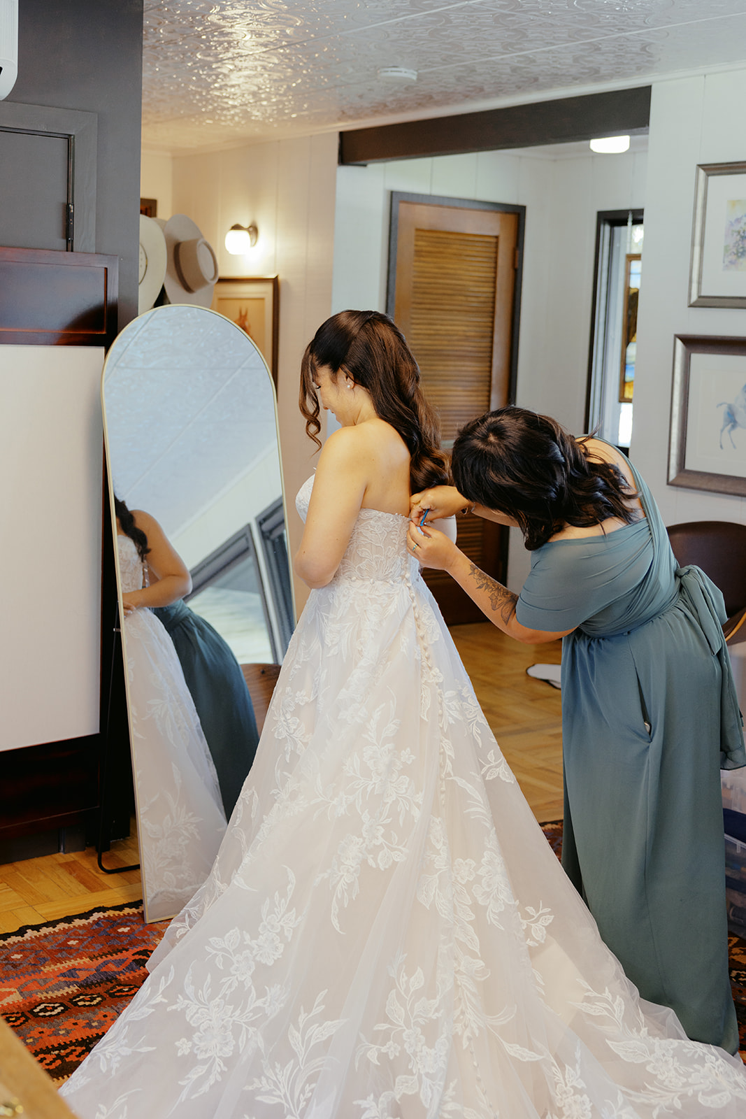 Rachel’s lace wedding dress being fastened during preparations