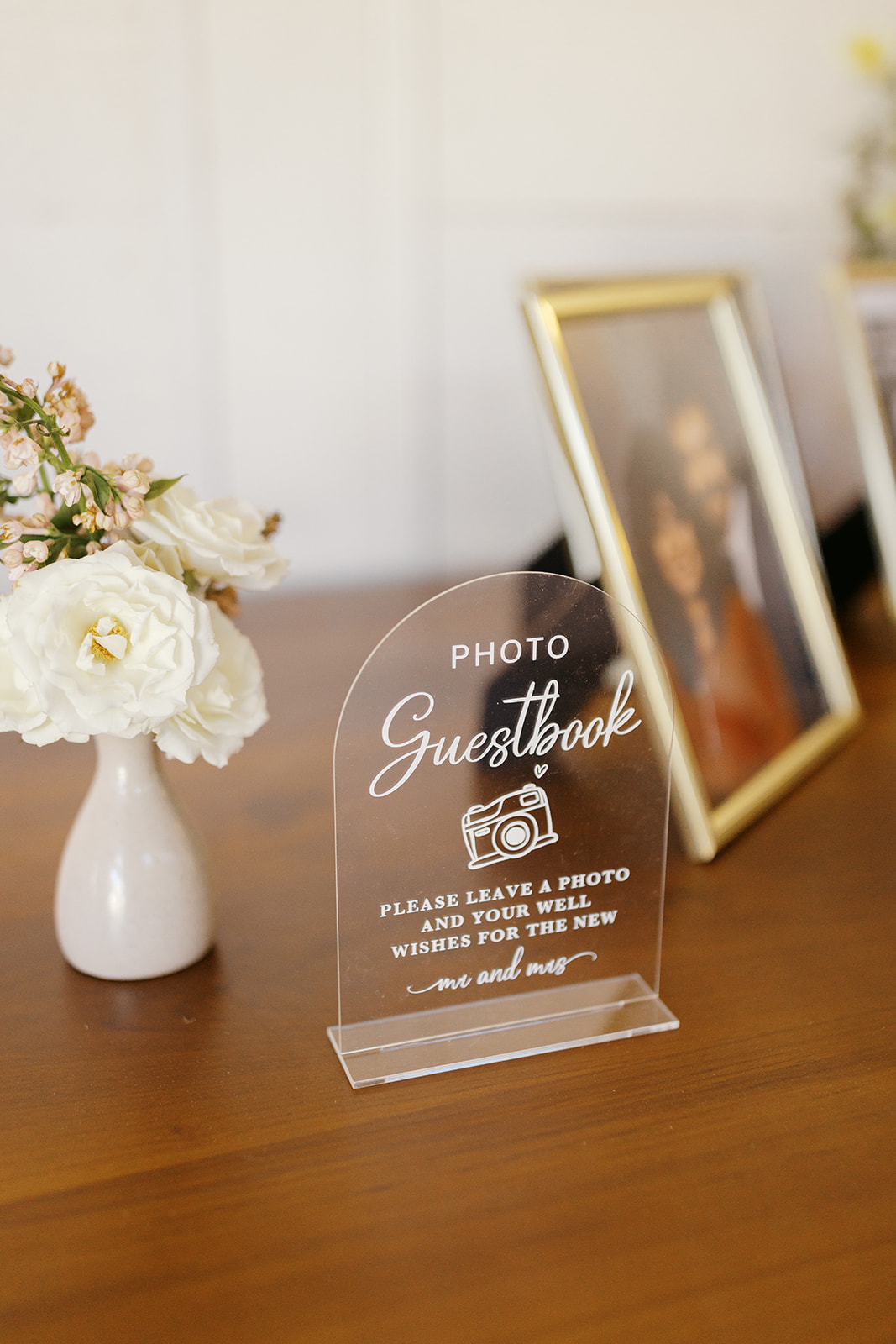 Acrylic photo guestbook sign beside flowers and framed photographs