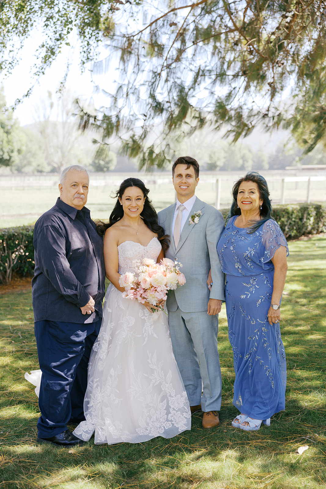 Rachel and Damien posing with family beneath the trees