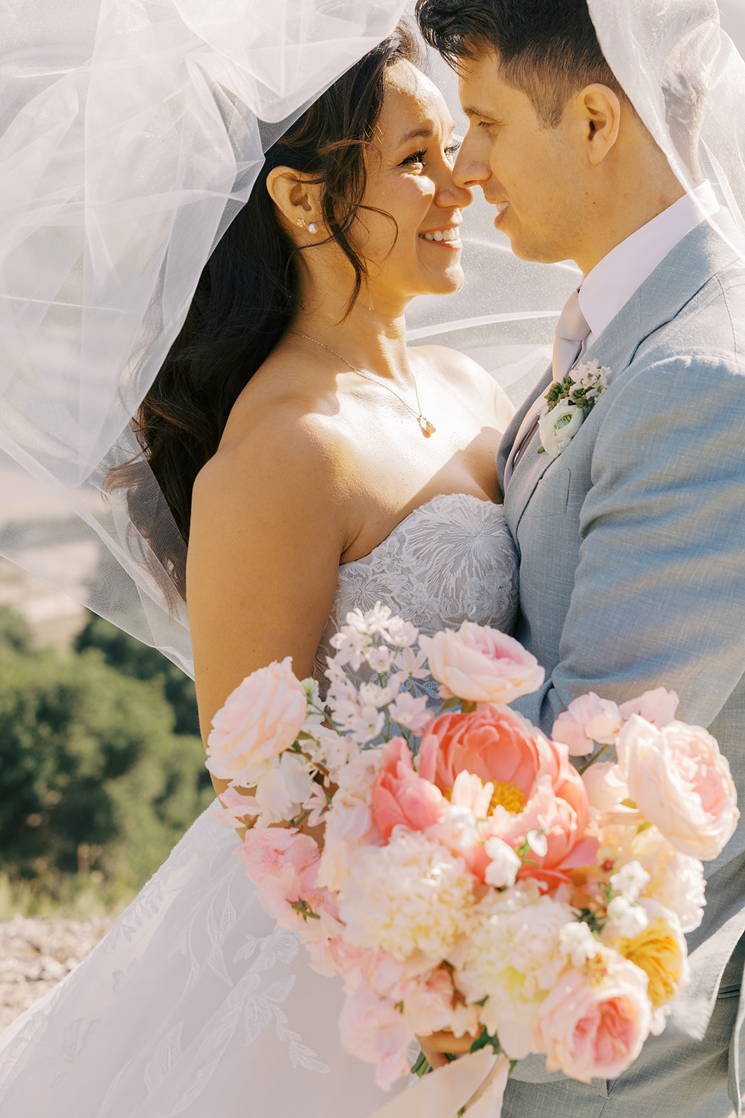 Rachel and Damien smiling beneath the bridal veil