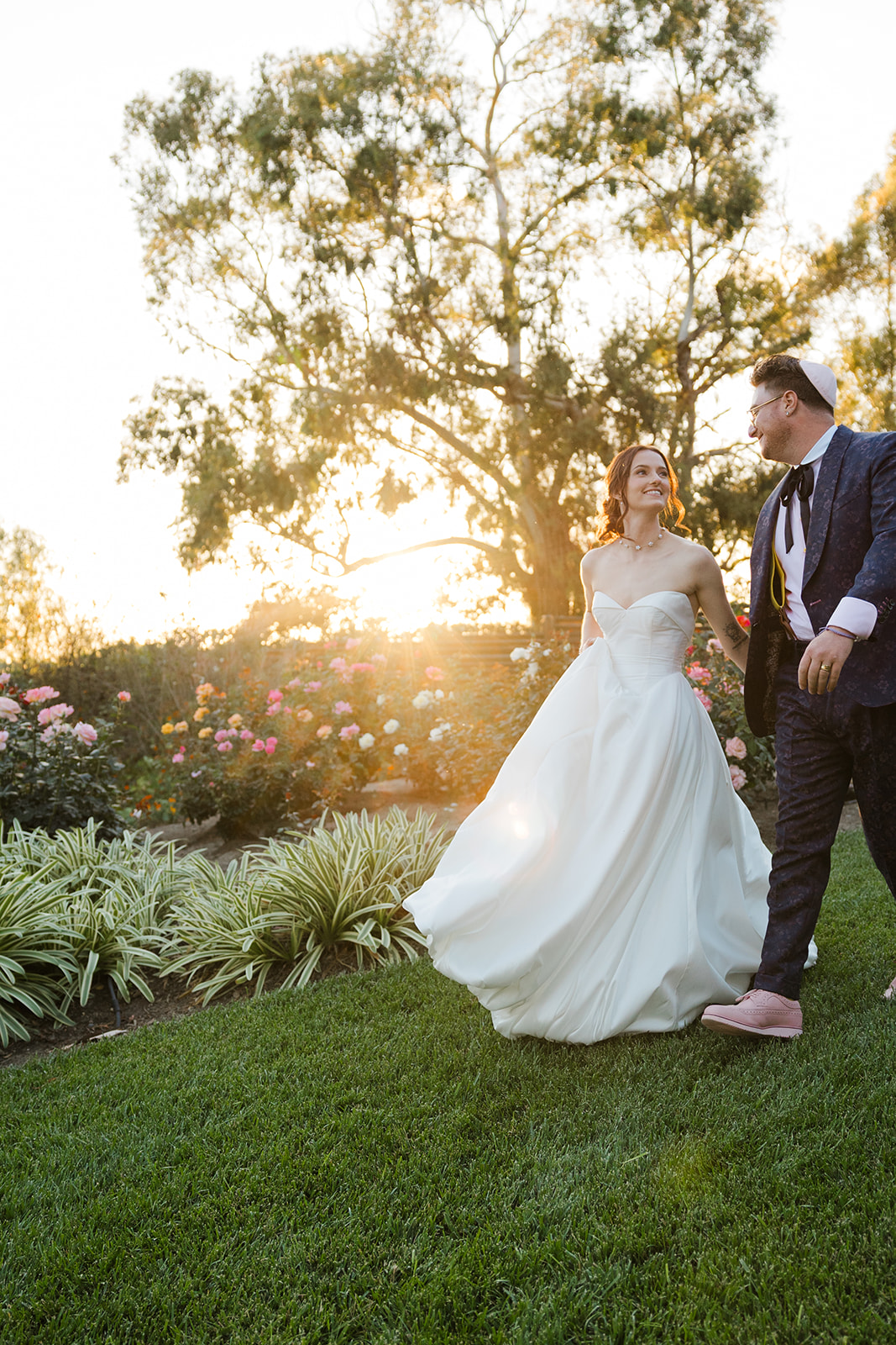 Jordan and Sara holding hands beside roses at golden hour