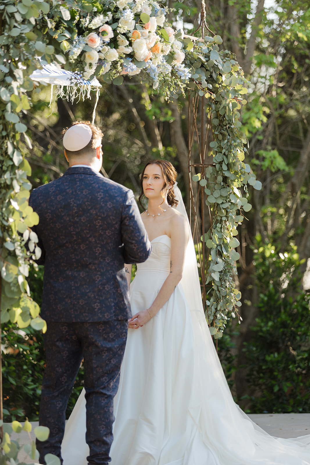Sara looking at Jordan beneath the flower-covered chuppah