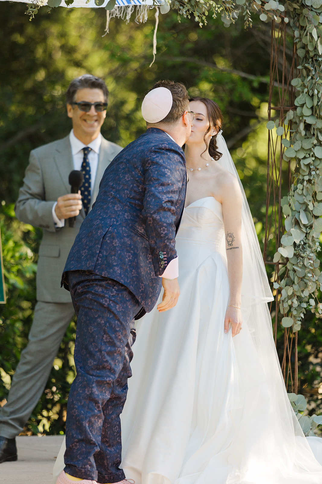 Jordan and Sara sharing their first kiss beneath the floral chuppah