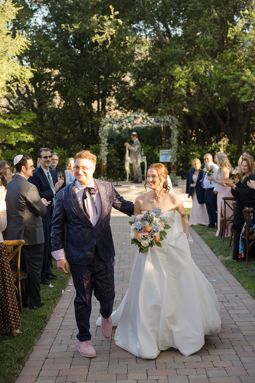 Jordan and Sara smiling as they walk back down the garden aisle